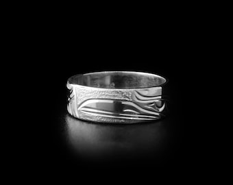 May include: A silver ring with a carved design of a stylized bird or animal. The ring is wide and has a smooth, polished finish.