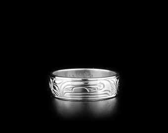 May include: A silver ring with a detailed carved design. The design features a stylized animal or bird motif.