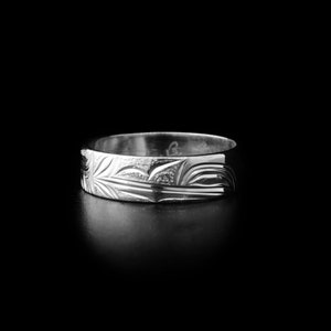 May include: A silver ring with an engraved design. The ring features a detailed pattern of stylized leaves and curved lines. The ring is set against a black background, highlighting its metallic sheen. The ring's width is approximately 0.64 cm.