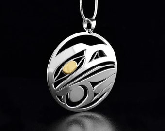 May include: A silver pendant necklace with a circular design featuring a stylized bird with a gold eye. The pendant is on a silver chain.