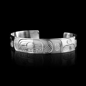 Op de afbeelding: Een zilveren manchetarmband met ingewikkelde gegraveerde ontwerpen. De armband heeft een centraal motief van een gestileerde dierfiguur, omringd door geometrische patronen. Het gepolijste metaal reflecteert licht, wat het gedetailleerde vakmanschap benadrukt.