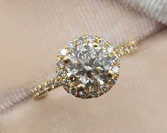 May include: A gold engagement ring with a round center diamond surrounded by a halo of smaller diamonds. The ring is set in a yellow gold band.