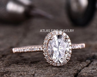 May include: A rose gold engagement ring with an oval-shaped center stone surrounded by a halo of smaller diamonds. The band is also set with smaller diamonds.