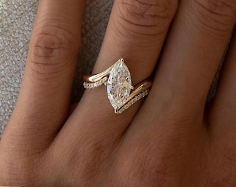 Peut inclure: Bague de fiançailles en or avec un diamant taille marquise. La bague présente un grand diamant clair en son centre, serti dans un design incurvé unique. De petits diamants sont sertis le long de la bande, ajoutant de l'éclat. La bague est sur un doigt.