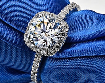 May include: A silver engagement ring with a large, round, clear diamond center stone surrounded by a halo of smaller diamonds. The band is also set with smaller diamonds.