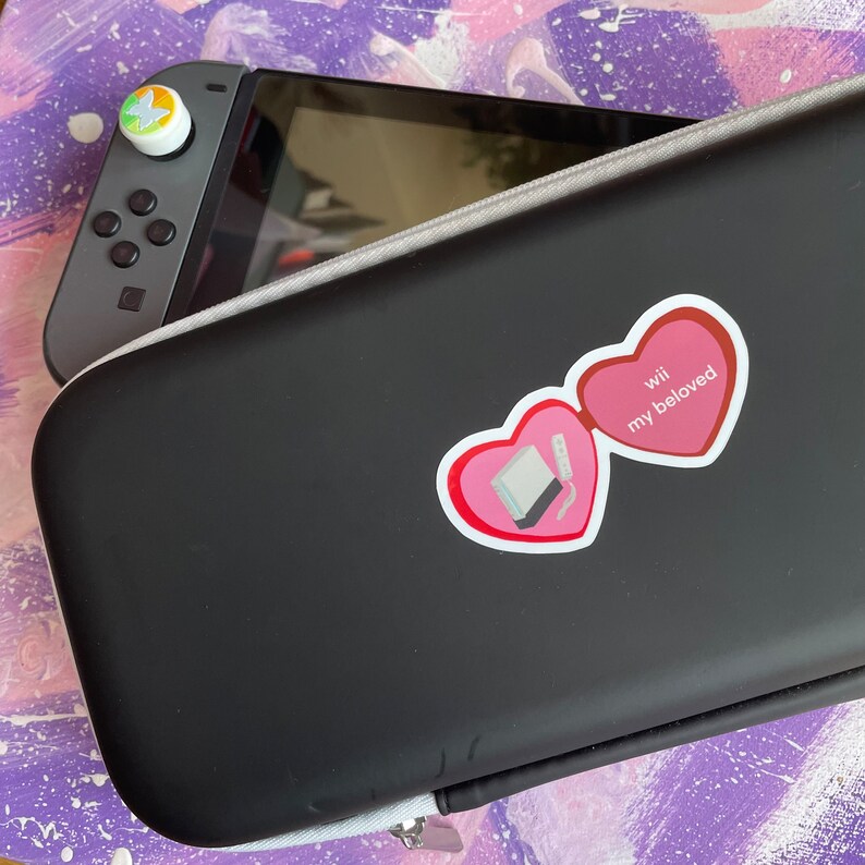 May include: A black Nintendo Wii console case with a pink heart sticker that says "Wii my beloved".