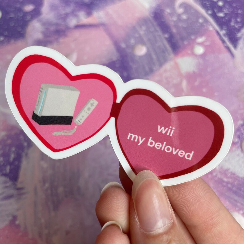 May include: A sticker with two pink hearts. One heart has a white Nintendo Wii console and a white remote. The other heart has the text "Wii my beloved".
