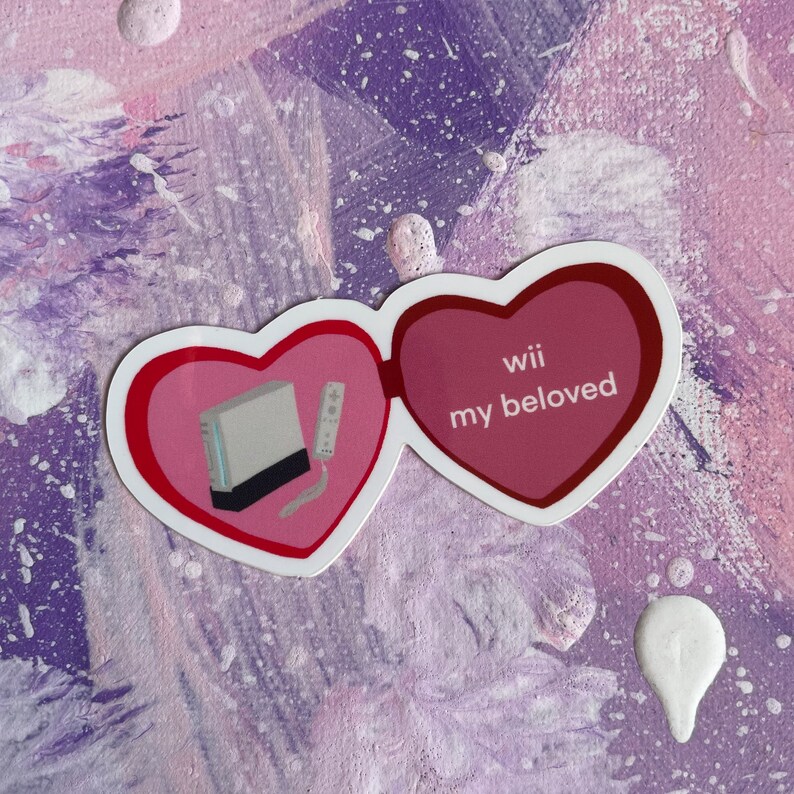 May include: A pink heart-shaped sticker with a white Nintendo Wii console and a white remote inside. The other heart says "Wii my beloved".