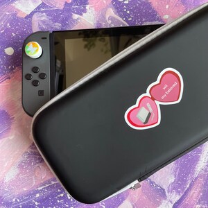 May include: A black Nintendo Switch carrying case with a pink heart sticker that says "Wii my beloved".