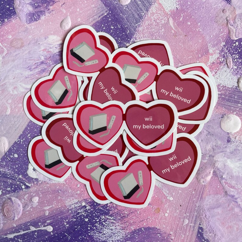 May include: A pile of pink and red heart-shaped stickers with the text "Wii my beloved" on each sticker. The stickers feature a cartoon image of a Nintendo Wii console and controller.