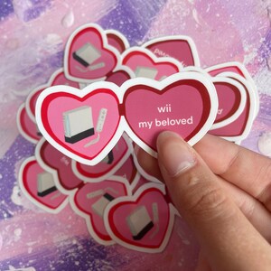May include: A set of pink heart-shaped stickers with a white Nintendo Wii console and remote inside one heart and the text "wii my beloved" inside the other heart.