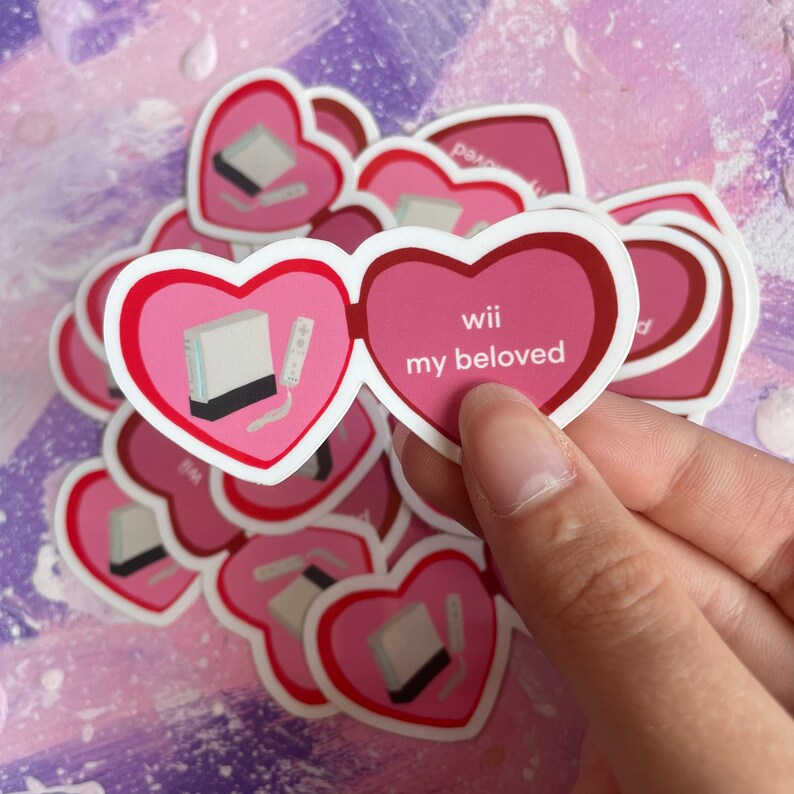 May include: A set of pink heart-shaped stickers with a white Nintendo Wii console and remote inside one heart and the text "wii my beloved" inside the other heart.