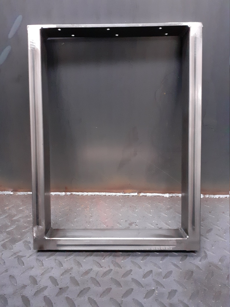 May include: A silver metal frame with a rectangular shape. The frame is made of thick metal and has a welded construction. The frame is sitting on a gray textured surface.