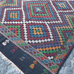 May include: A black and white rug with a colourful geometric pattern. The rug has a fringe border and is made of wool.