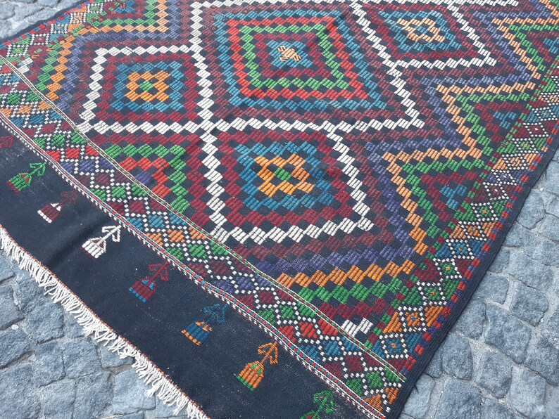 May include: A black and white rug with a colourful geometric pattern. The rug has a fringe border and is made of wool.