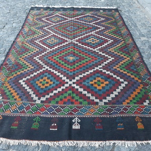 May include: A colourful, hand-woven rug with a geometric pattern in shades of red, blue, green, yellow, and white. The rug has a black background and a fringe border.
