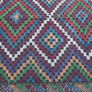 May include: A colourful rug with a geometric pattern of squares and diamonds in shades of red, green, blue, white and black.