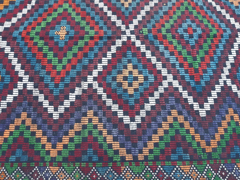 May include: A colourful rug with a geometric pattern of squares and diamonds in shades of red, green, blue, white and black.