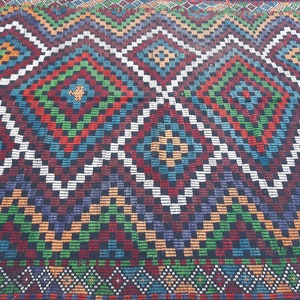 May include: A colourful rug with a geometric pattern in shades of red, green, blue, white, and black. The rug has a diamond pattern with smaller squares within the diamonds.