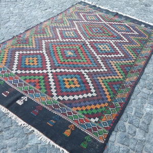 May include: A black and white rug with a geometric pattern in shades of red, green, blue, and yellow. The rug has a fringed border.