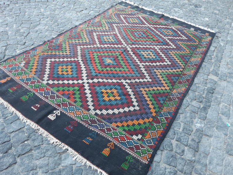 May include: A black and white rug with a geometric pattern in shades of red, green, blue, and yellow. The rug has a fringed border.