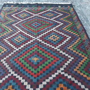May include: A colourful rug with a geometric pattern in shades of red, green, blue, white, and black. The rug has a diamond-shaped design with intricate details.