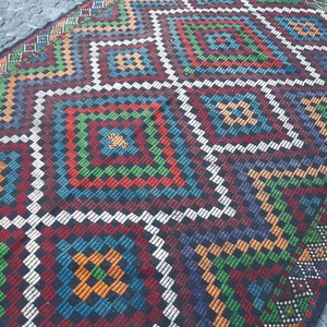 May include: A colourful rug with a geometric pattern in shades of red, green, blue, orange, and white. The rug has a traditional design with a repeating diamond pattern.