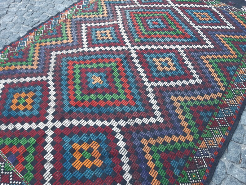 May include: A colourful rug with a geometric pattern in shades of red, green, blue, orange, and white. The rug has a traditional design with a repeating diamond pattern.