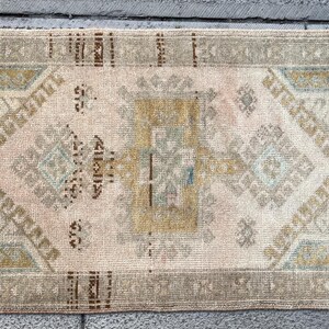 May include: A small, rectangular rug with a faded, cream-colored background and a geometric pattern in shades of brown, beige, and blue.