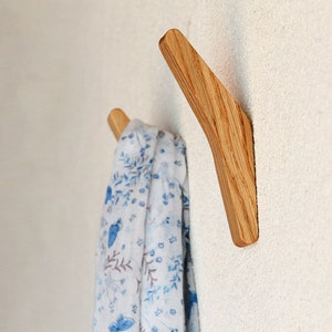 May include: A wooden wall hook with a curved design. A white scarf with a blue floral pattern is hanging on the hook.
