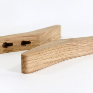 May include: Two wooden wall hooks with a curved shape and a natural wood finish. The hooks have two holes each for hanging items.