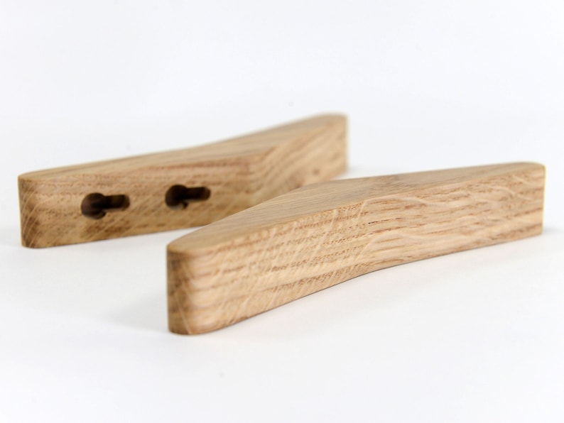 May include: Two wooden wall hooks with a curved shape and a natural wood finish. The hooks have two holes each for hanging items.