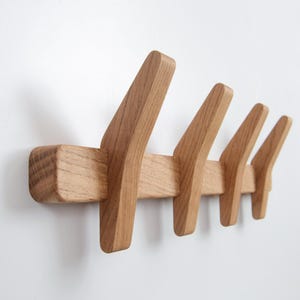 May include: A wooden wall-mounted coat rack with five hooks. The hooks are angled and made of solid wood.