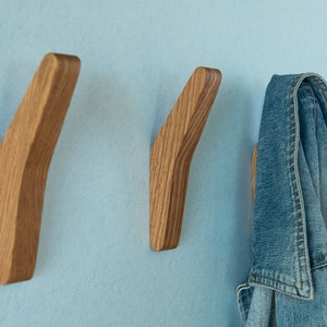 May include: Three wooden wall hooks with a curved design. One hook has a blue denim jacket hanging on it.