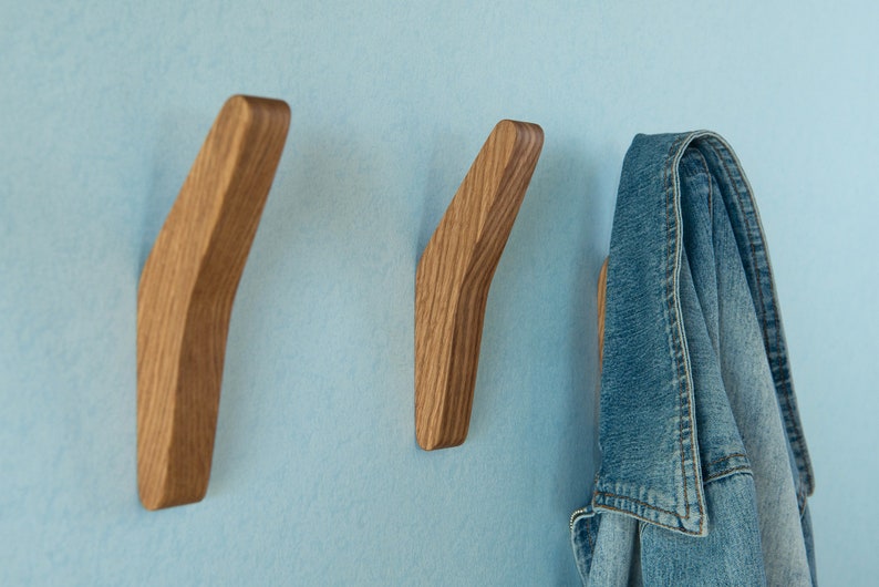 May include: Three wooden wall hooks with a curved design. One hook has a blue denim jacket hanging on it.