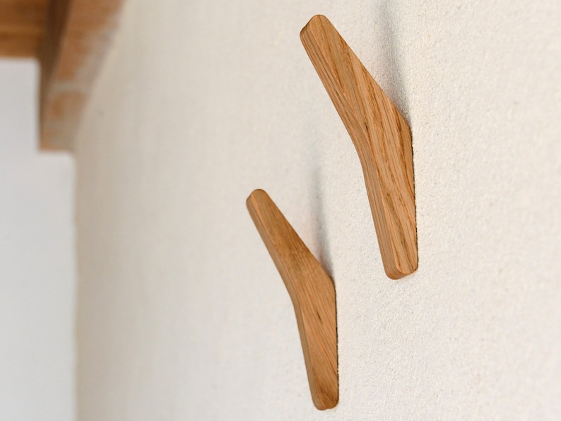 May include: Two wooden wall hooks in a light brown color, mounted on a white wall. The hooks are angled and have a curved shape.