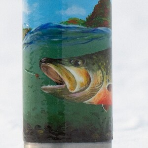 May include: A stainless steel tumbler with a detailed illustration of a fish underwater. The design includes a blue sky, green water, and a fish with orange and brown accents. The tumbler has a silver base.