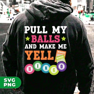 Könnte beinhalten: Ein schwarzer Hoodie mit dem Text "PULL MY ★BALLS★ AND MAKE ME YELL" und einer Reihe bunter Bingokugeln.