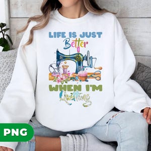Peut inclure: Sweat-shirt blanc avec un motif coloré d'une machine à coudre vintage, des bobines de fil et des fleurs. Le texte dit "LIFE IS JUST Better WHEN I'M Quilting."