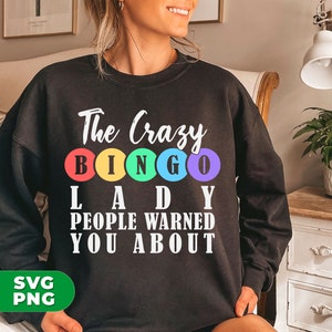 Könnte beinhalten: Schwarzes Sweatshirt mit weißem Text, der "The Crazy Bingo Lady People Warned You About" lautet. Der Text ist von fünf bunten Kreisen umgeben.