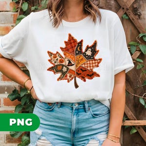 May include: A white short-sleeved t-shirt featuring a large central graphic of a maple leaf composed of various patchwork segments. The segments display autumn and Halloween motifs including pumpkins, a witch hat, a ghost, bats, and stars.