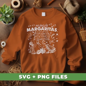 May include: A brown sweatshirt with a white design that says "midnight margaritas" with a whimsical illustration of a potion bottle, a frog, and a feather. The text reads "Eye of neat, and fire of frag, Wind of bit, and tongue of day, Folder's fork, and blind-worn's sling, Lound's lig, and howht's wing, For a charm of powerful trouble, Like a bel-broth boil and bubble."