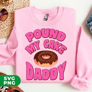 Puede incluir: Sudadera rosa con el texto "Pound My Cake Daddy" en letras rosas y una dona de chocolate con chispas.