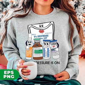 May include: Gray sweatshirt with a graphic of a medical IV bag and three vials with cartoon faces. The text "PRESSURE IS ON" is printed below the graphic.
