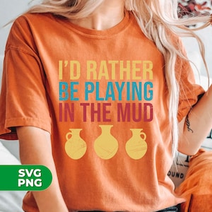 May include: Orange t-shirt with the text "I'd rather be playing in the mud" in a vintage style font. Three yellow stylized pottery jars are below the text.