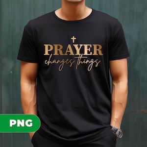 Può includere: T-shirt nera con testo dorato "PRAYER changes things" e una croce sopra la parola "PRAYER". Il testo è in grassetto, senza grazie, mentre "changes things" è in corsivo. La maglietta è a girocollo.