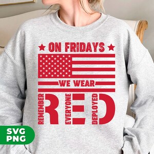 May include: Gray sweatshirt with a red, white, and blue American flag design. The text "On Fridays We Wear Red" is written below the flag. The words "Remember", "Everyone", "Deployed" are written vertically in red.