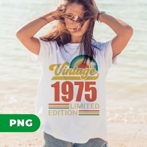 May include: White t-shirt with a retro design featuring the words "Vintage 1975 Limited Edition" in yellow, red, and green. The design includes a rainbow and palm trees. The shirt is being worn on a beach.