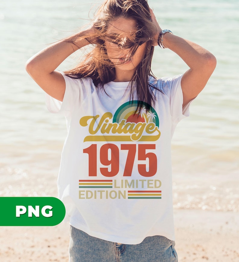 May include: White t-shirt with a retro design featuring the words "Vintage 1975 Limited Edition" in yellow, red, and green. The design includes a rainbow and palm trees. The shirt is being worn on a beach.