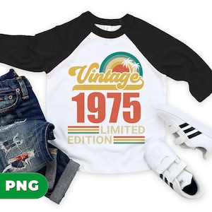 May include: White and black raglan style t-shirt with the text "Vintage 1975 Limited Edition" in orange and yellow. The shirt is paired with blue jeans and white sneakers with black stripes.